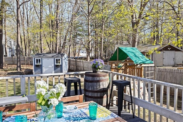 wooden terrace with a storage shed, a fenced backyard, and a playground