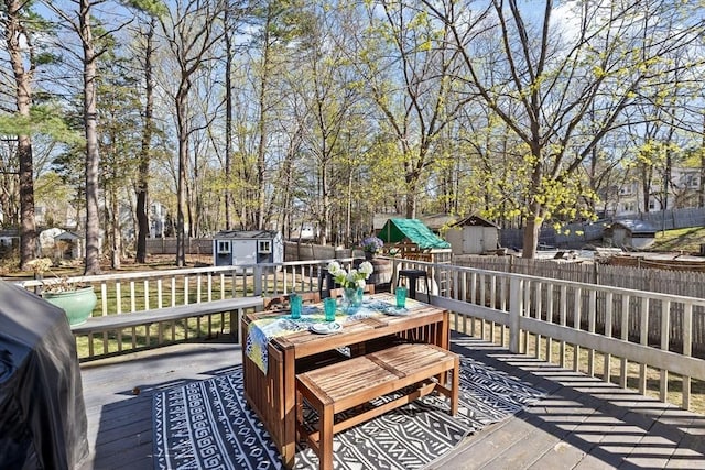 wooden deck featuring a storage shed, outdoor dining space, an outdoor structure, and a fenced backyard