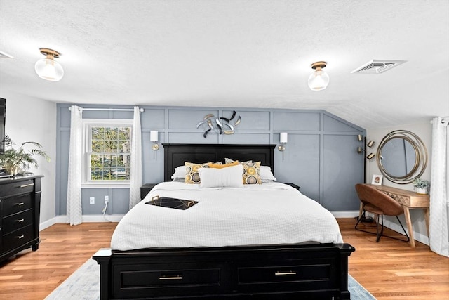 bedroom with a textured ceiling, baseboards, visible vents, and light wood-style floors