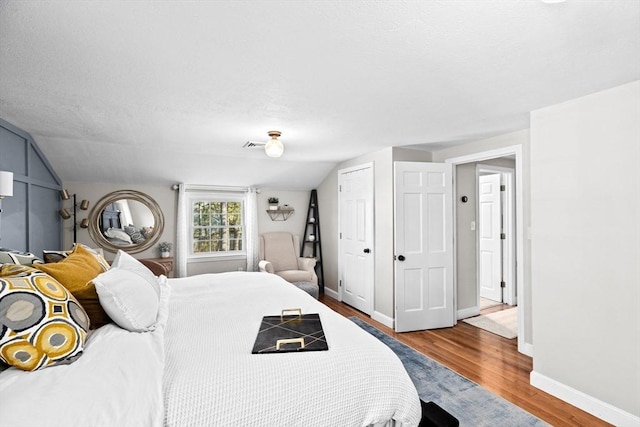 bedroom featuring baseboards, vaulted ceiling, wood finished floors, and visible vents