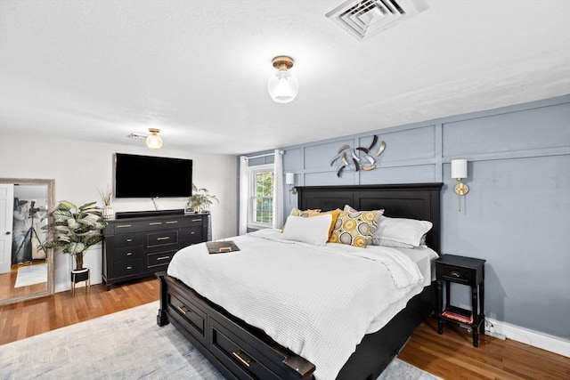 bedroom with baseboards, wood finished floors, and visible vents