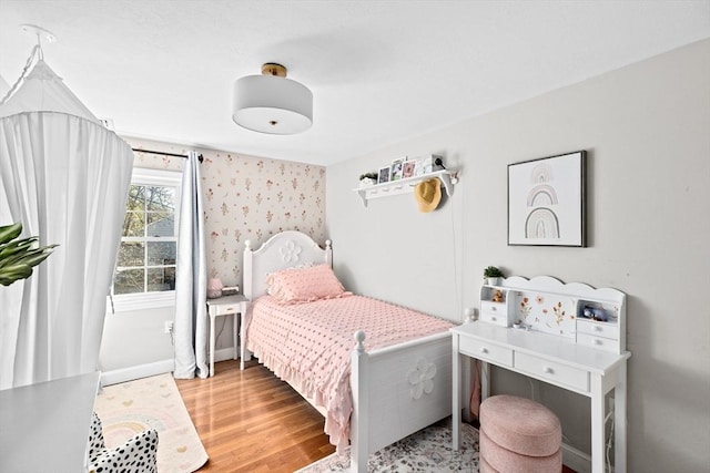 bedroom with baseboards, wood finished floors, and wallpapered walls