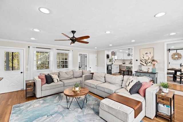 living room with a ceiling fan, wainscoting, ornamental molding, recessed lighting, and light wood-style flooring