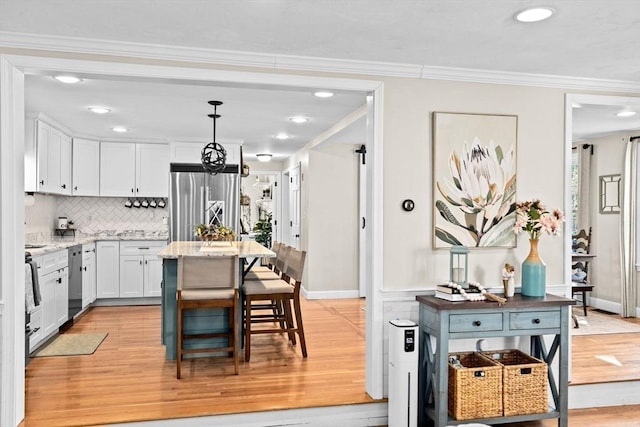 kitchen with a kitchen bar, stainless steel refrigerator, white cabinets, light wood-style floors, and ornamental molding