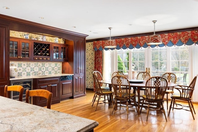 dining space with wet bar, ornamental molding, and light wood-type flooring