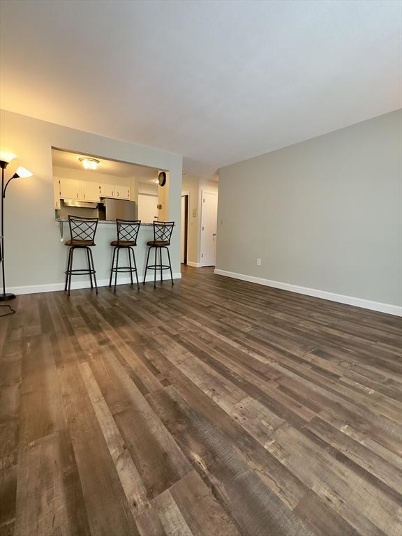 unfurnished living room featuring dark wood-style floors and baseboards