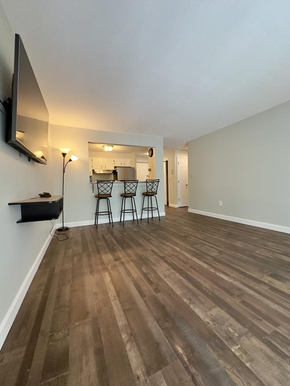 unfurnished living room featuring dark wood-type flooring and baseboards