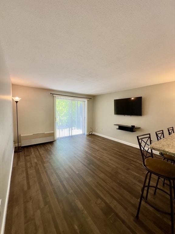 unfurnished living room with baseboards, a textured ceiling, a baseboard heating unit, and dark wood-style flooring