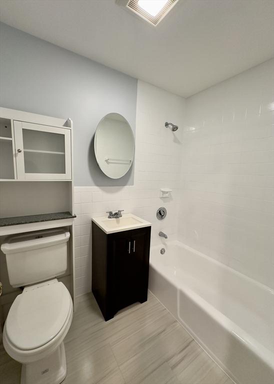 bathroom featuring tile walls, shower / bathtub combination, visible vents, toilet, and vanity