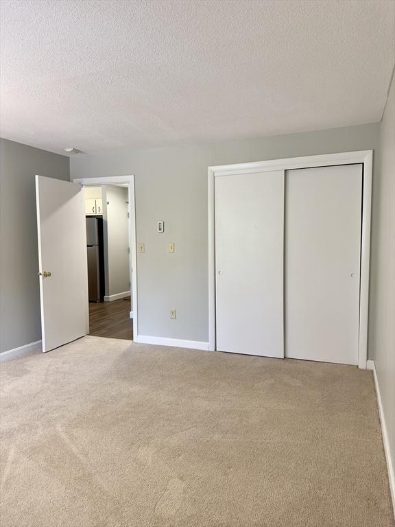 unfurnished bedroom with carpet, a closet, freestanding refrigerator, a textured ceiling, and baseboards