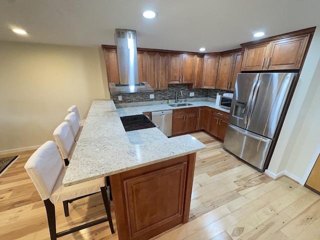 kitchen with a peninsula, light stone counters, island exhaust hood, a sink, and appliances with stainless steel finishes