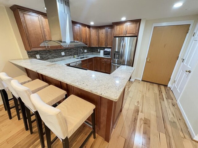 kitchen featuring appliances with stainless steel finishes, a sink, light wood-style floors, a peninsula, and island exhaust hood