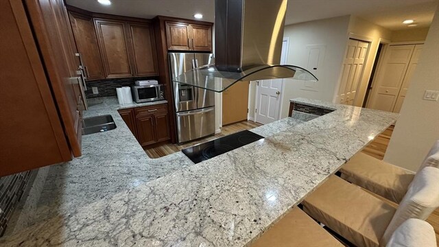 kitchen featuring island range hood, appliances with stainless steel finishes, light stone counters, light wood-style floors, and recessed lighting