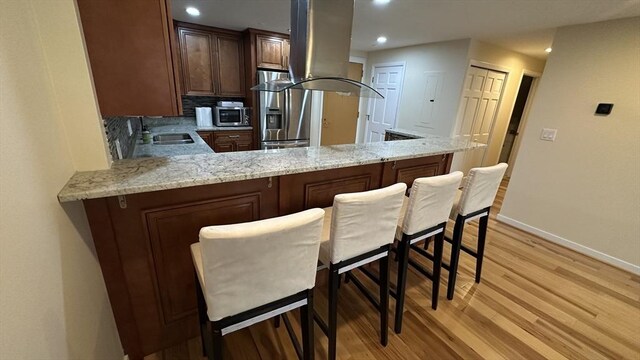 kitchen with a peninsula, baseboards, island range hood, a sink, and appliances with stainless steel finishes