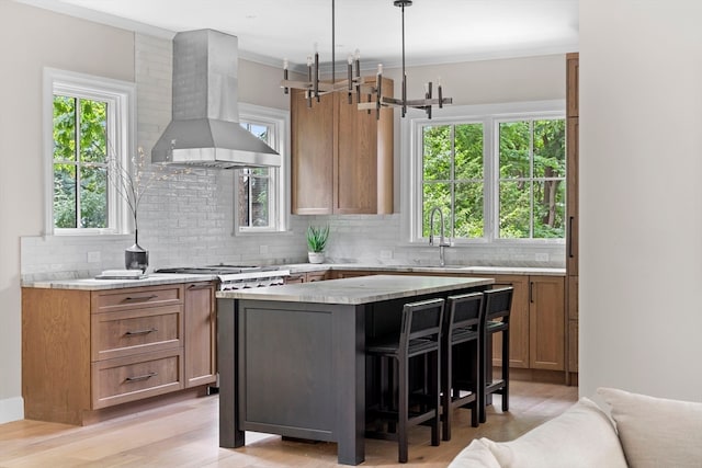 kitchen featuring a wealth of natural light, wall chimney exhaust hood, a kitchen island, light hardwood / wood-style floors, and sink