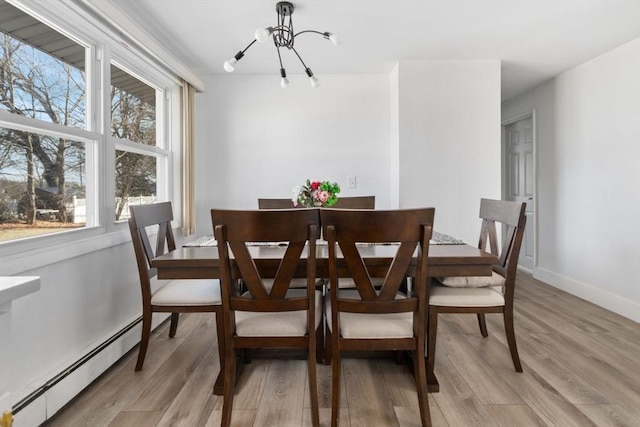 dining space featuring light wood-type flooring, a baseboard radiator, a healthy amount of sunlight, and a notable chandelier