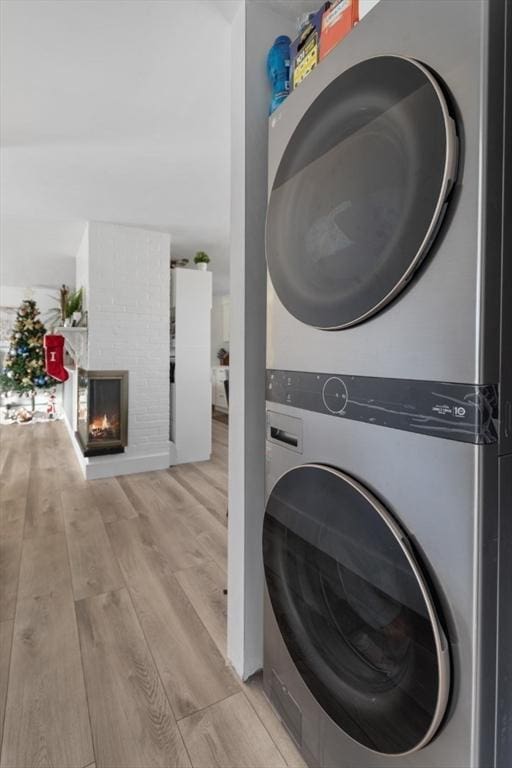 washroom featuring stacked washing maching and dryer, light hardwood / wood-style flooring, and a brick fireplace