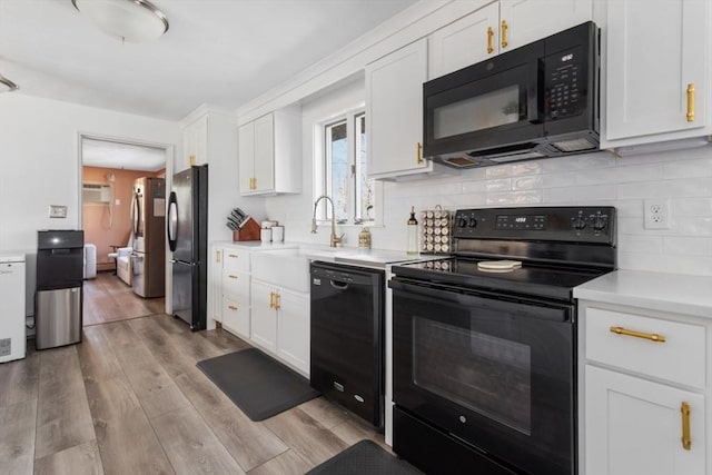 kitchen with white cabinets, light hardwood / wood-style floors, a wall unit AC, and black appliances