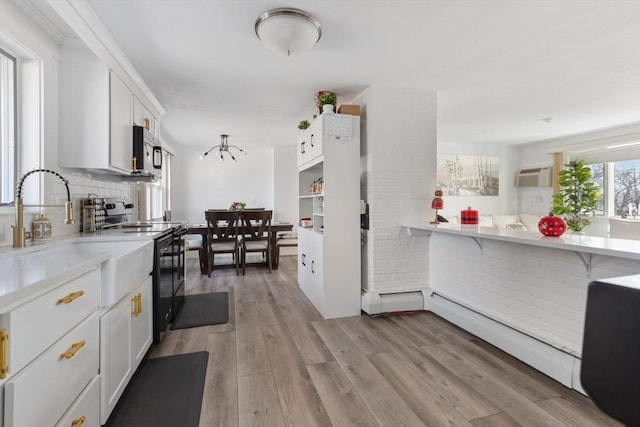 kitchen featuring backsplash, black range oven, sink, light hardwood / wood-style floors, and white cabinetry