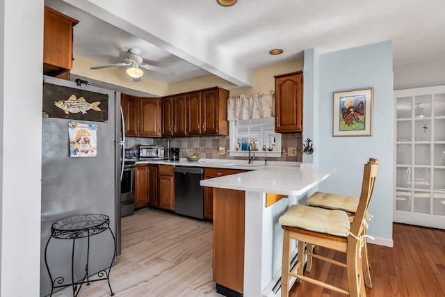 kitchen featuring decorative backsplash, a kitchen breakfast bar, a peninsula, light countertops, and stainless steel appliances