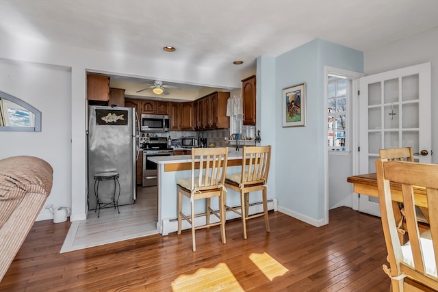 kitchen featuring a breakfast bar area, a baseboard radiator, appliances with stainless steel finishes, light wood-style floors, and a peninsula