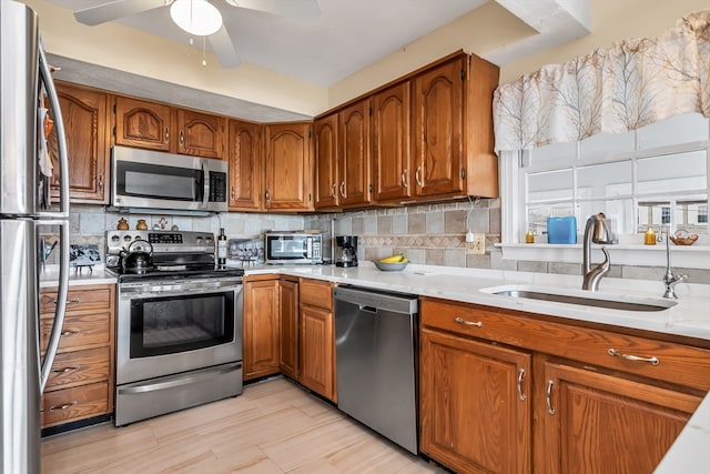 kitchen with brown cabinetry, a sink, stainless steel appliances, light countertops, and backsplash