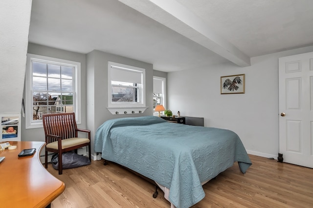 bedroom with light wood finished floors, beamed ceiling, baseboard heating, and baseboards