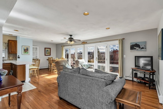 living room with a ceiling fan, french doors, light wood-style floors, a baseboard heating unit, and recessed lighting