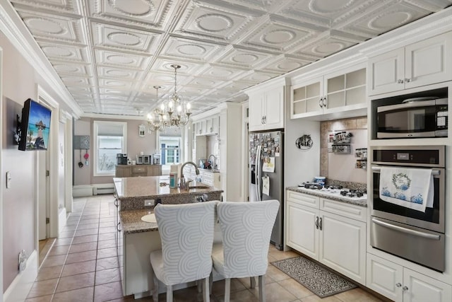 kitchen with an ornate ceiling, a notable chandelier, a kitchen island with sink, a warming drawer, and appliances with stainless steel finishes
