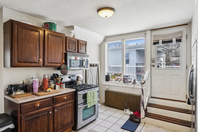 kitchen with radiator, appliances with stainless steel finishes, light tile patterned flooring, and light countertops