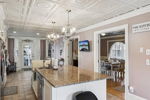 kitchen with a sink, a chandelier, a kitchen island with sink, stone countertops, and white cabinetry