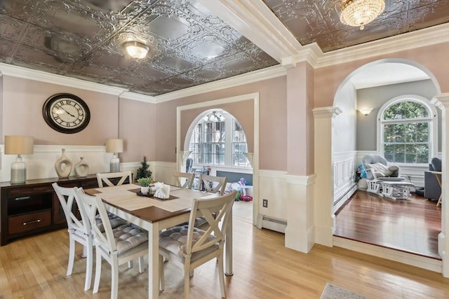 dining area featuring light wood-style flooring, arched walkways, an ornate ceiling, ornate columns, and a baseboard radiator