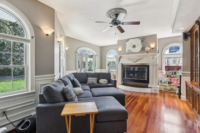 living area with a baseboard radiator, a ceiling fan, wood finished floors, and a healthy amount of sunlight