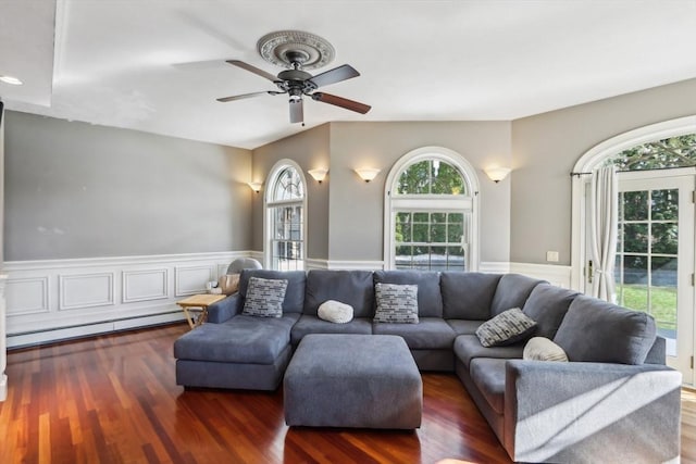 living room featuring a baseboard heating unit, wood finished floors, a healthy amount of sunlight, and wainscoting