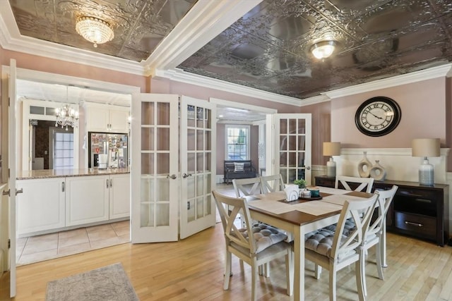 dining room with light wood-type flooring, french doors, a chandelier, and an ornate ceiling