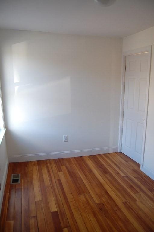 empty room with wood-type flooring, visible vents, and baseboards