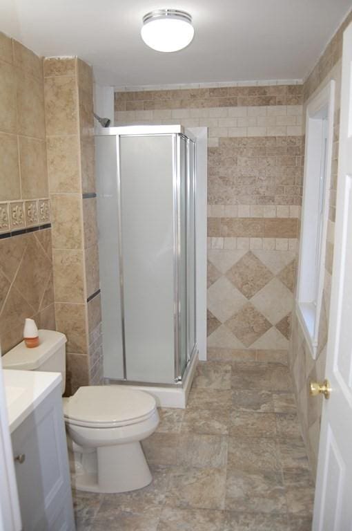 full bath featuring toilet, a stall shower, tile walls, and vanity