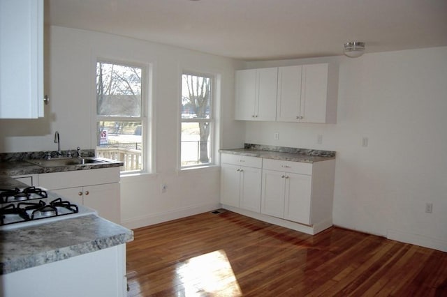 kitchen featuring a sink, wood finished floors, white cabinetry, and baseboards