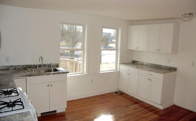 kitchen featuring white cabinets, a sink, wood finished floors, baseboards, and white gas range oven