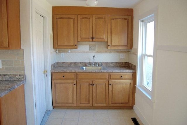 kitchen featuring brown cabinetry, light tile patterned flooring, a sink, and backsplash
