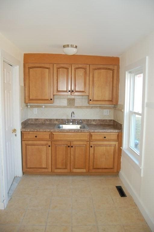 kitchen with brown cabinetry, visible vents, a sink, and backsplash