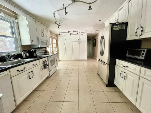 kitchen featuring white appliances, dark countertops, light tile patterned flooring, and a healthy amount of sunlight