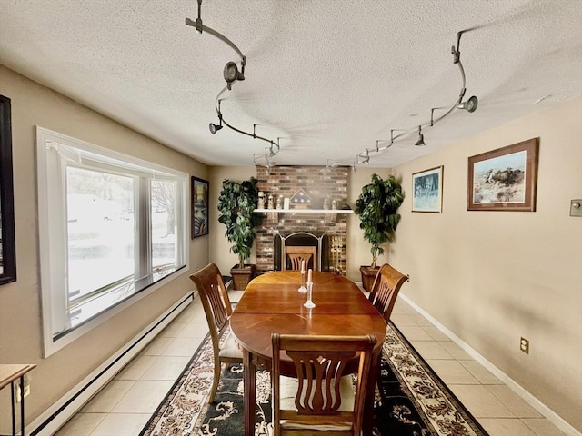 dining space with a textured ceiling, a baseboard radiator, light tile patterned flooring, and a brick fireplace