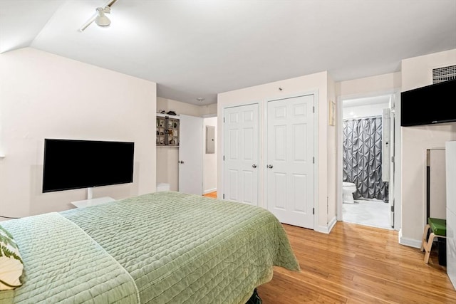 bedroom with light wood-type flooring, multiple closets, baseboards, connected bathroom, and lofted ceiling