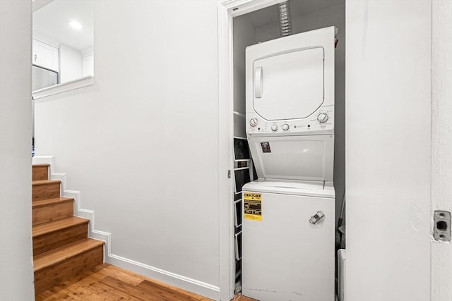 laundry room with stacked washer / drying machine, wood finished floors, and baseboards