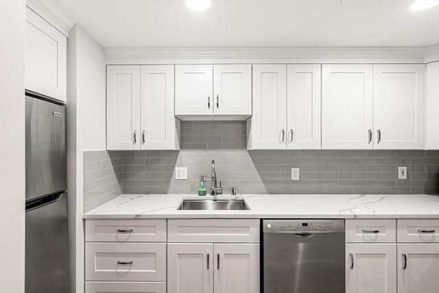 kitchen featuring stainless steel appliances, a sink, white cabinets, tasteful backsplash, and light stone counters