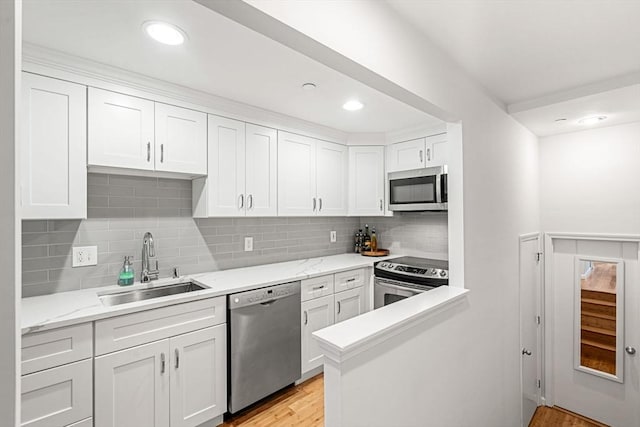 kitchen with stainless steel appliances, a sink, white cabinetry, light wood-type flooring, and recessed lighting