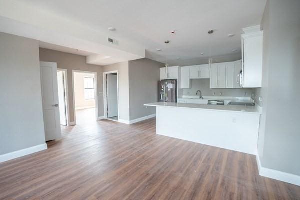 kitchen with decorative light fixtures, light hardwood / wood-style floors, stainless steel refrigerator with ice dispenser, kitchen peninsula, and white cabinets