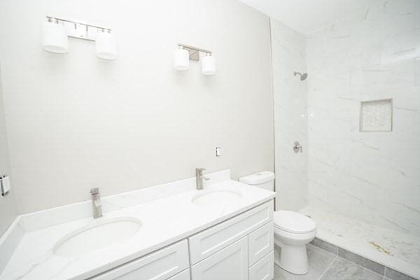 bathroom with toilet, a tile shower, tile patterned floors, and vanity