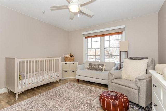 bedroom with hardwood / wood-style flooring, a nursery area, and ceiling fan